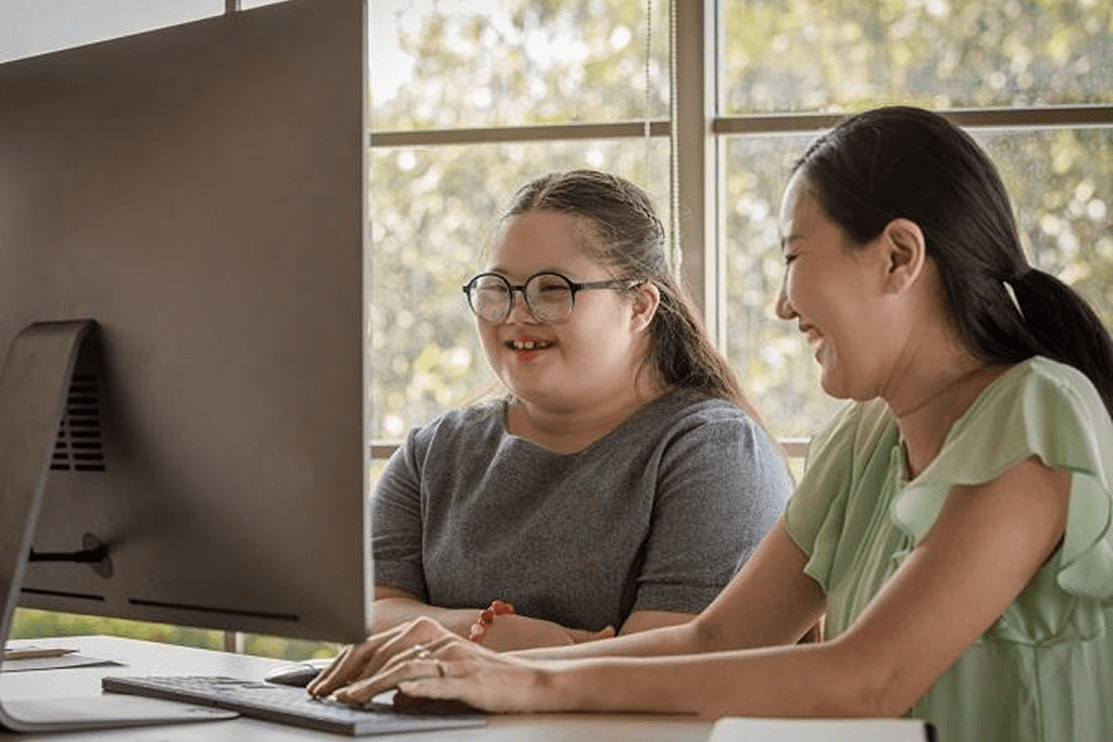 Two women smiling at a computer screen.