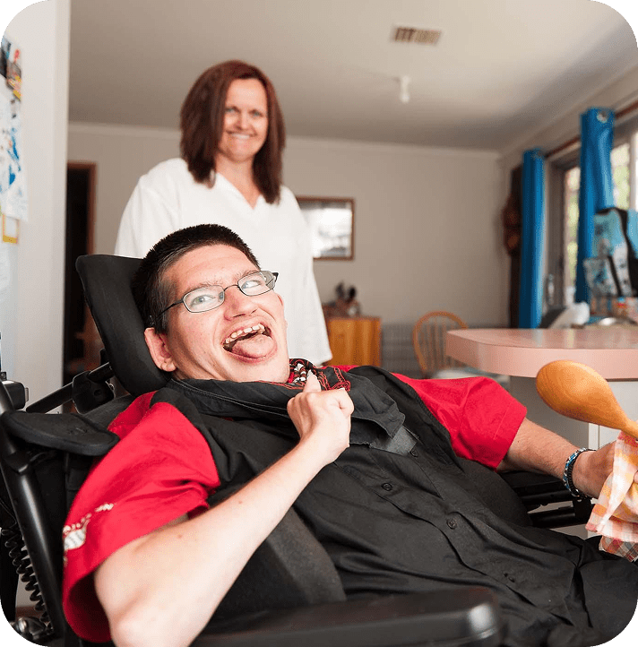Person in wheelchair smiling with caregiver nearby.