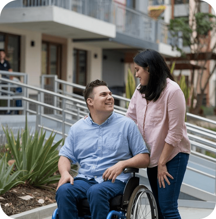 Man in wheelchair smiling at woman outside.